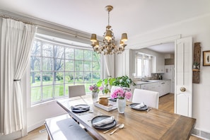 A dining area with a wooden table set for four, a chandelier, and a view of the garden through large windows. - Knoxville Area Getaway on 22 Acres w/ Pond Access! (Knoxville)