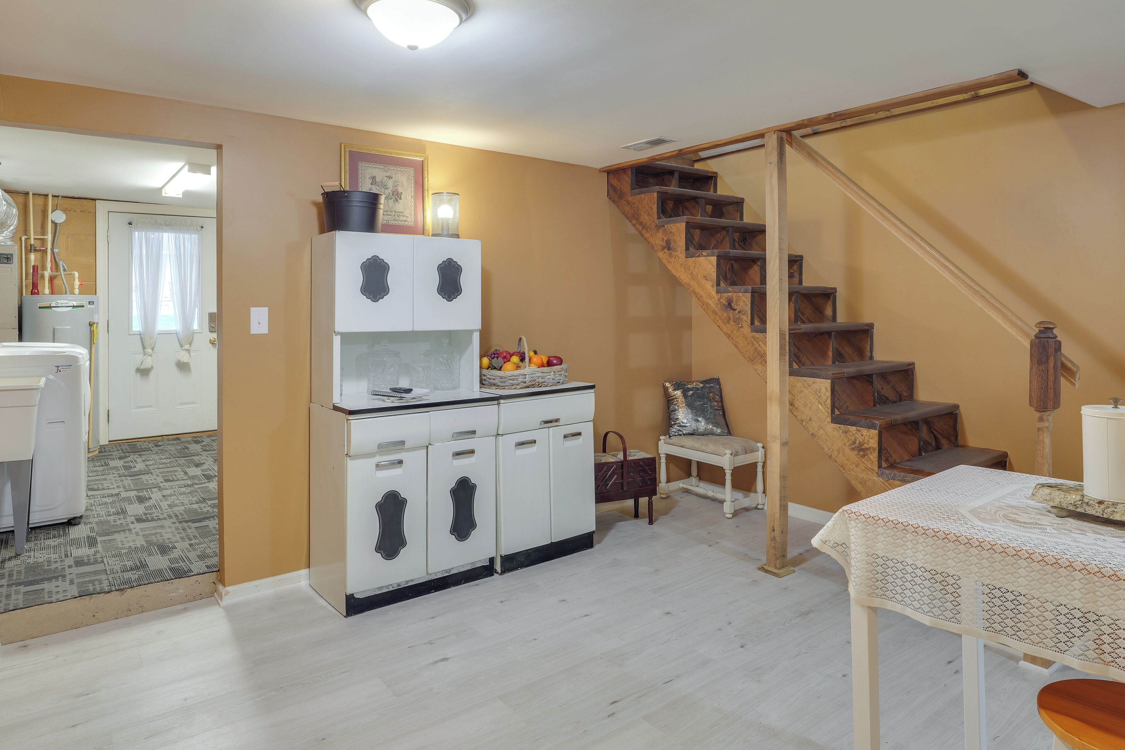 A kitchen with white cabinets, a wooden staircase, and a dining area with a table and chairs.