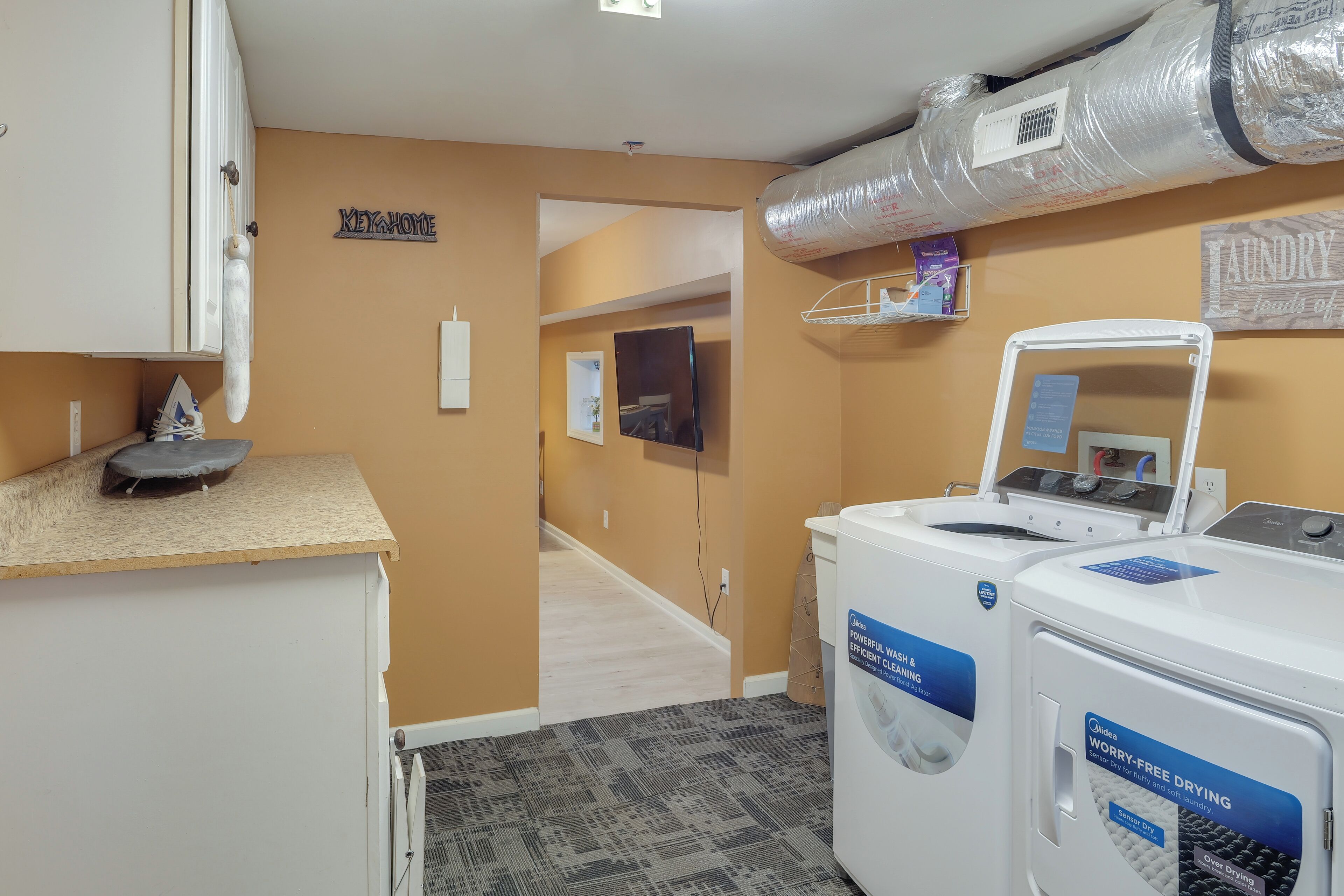 A laundry room with two front-loading washing machines, a dryer, and a small shelf with laundry supplies.