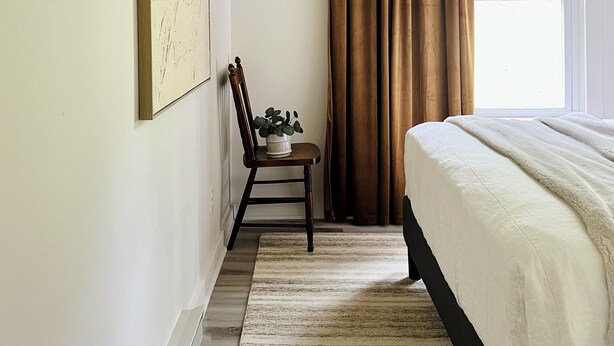 A bedroom with a bed, a chair with a plant, a window with curtains, and a painting on the wall. - HOOTING HAUS - HOT TUB - FIRE PIT - CABIN RETREAT (Port Matilda)