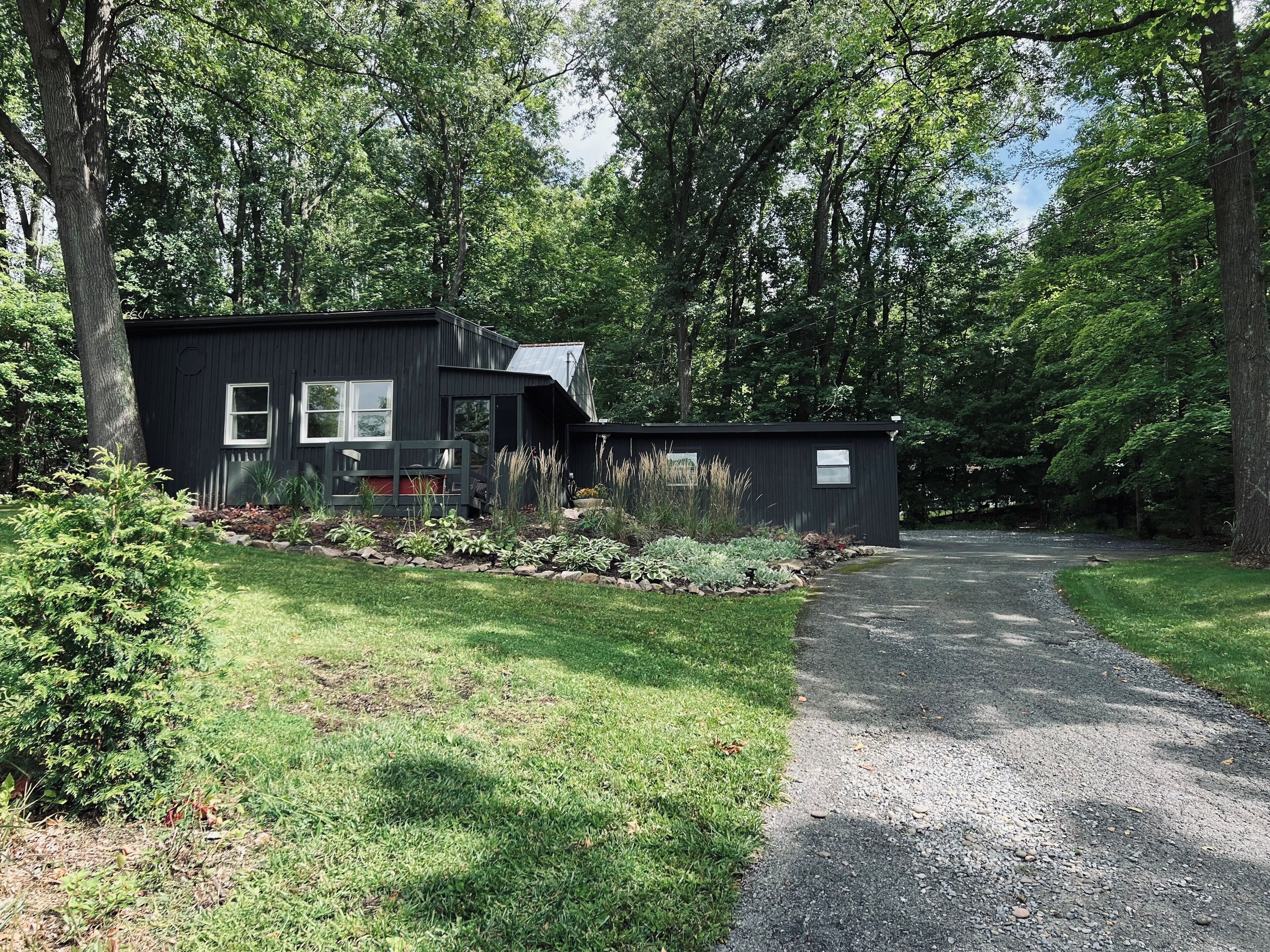 A modern two-story house with a gravel driveway leading to a wooden deck.