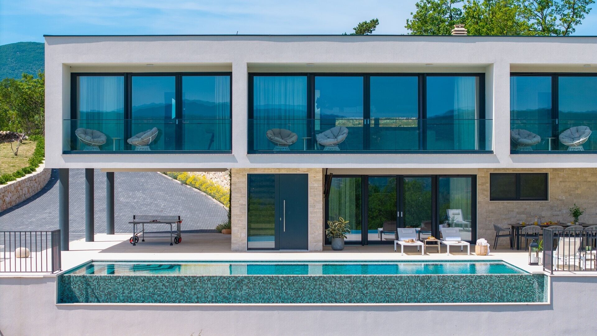 Una casa moderna de dos plantas con un amplio ventanal en el piso superior y una piscina en la planta baja.