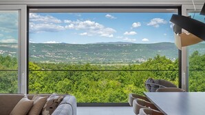 Een moderne woonkamer met een grote schuifdeur naar een balkon met een prachtig uitzicht op heuvels en een dorp.