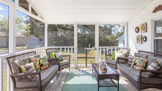 A covered porch with wicker furniture, a glass door, and a view of the backyard. - Adorable Chincoteague home by Seaside Vacations & Sales (Chincoteague Island)