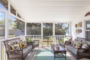 A covered porch with wicker furniture, a glass door, and a view of the backyard. - Adorable Chincoteague home by Seaside Vacations & Sales (Chincoteague Island)