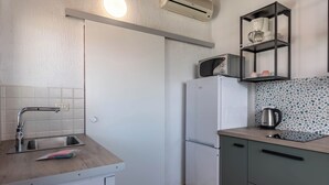 Cocina compacta con lavamanos, microondas, refrigerador y una repisa con tazas y tetera.
