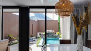 Ein modernes Interieur mit Essbereich, einem großen Fenster mit Blick auf Pool und Außenbereich sowie einer dekorativen Vase mit Pflanzen.