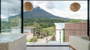 Ein modernes Hotelzimmer mit einer großen Glasdoor zu einem Balkon, einer Whirlpool und Blick auf einen Berg.
