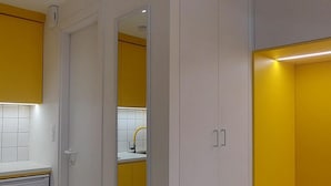 Une chambre avec un coin cuisine, un lit doté d’une tête de lit jaune et un miroir au mur.