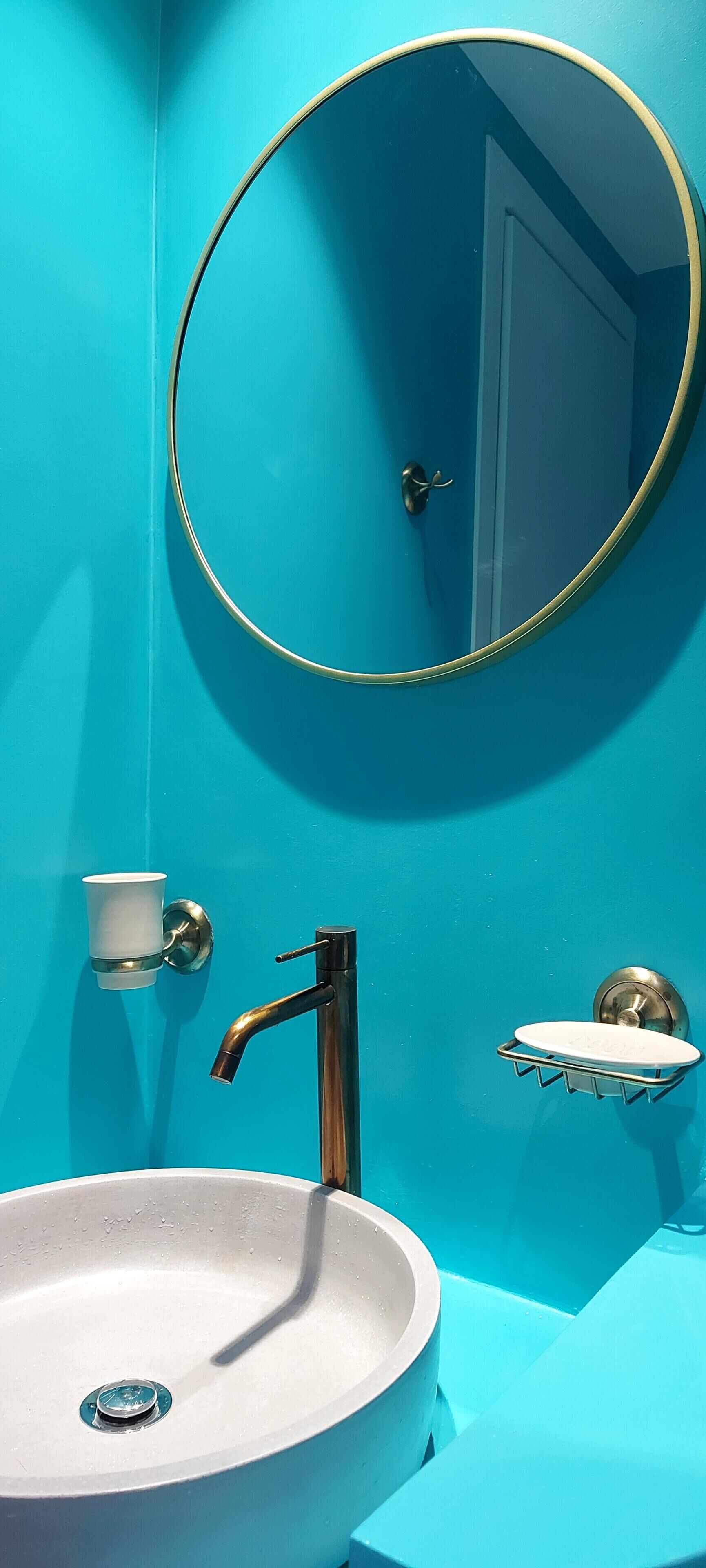 A bathroom with a white sink, a round mirror with a gold frame, a chrome faucet, and a small white cup holder.