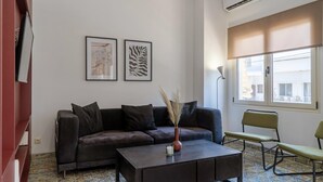 En moderne stue med sofa, sofabord og lænestol. To billeder hænger på væggen, og en klimaanlæg er monteret på væggen.