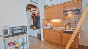 A kitchen with wooden cabinets, a microwave, and a wooden stool. - Studio Riffelsee (Zermatt)