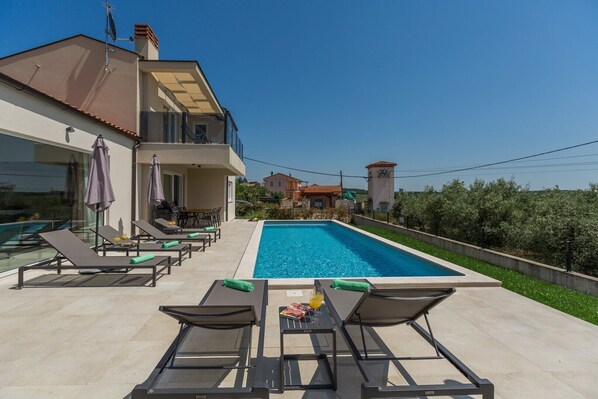 A modern house with a swimming pool, outdoor seating, and a clear view of the surrounding landscape.