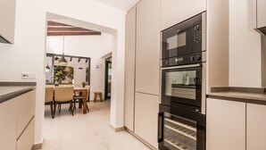 Une cuisine moderne dotée d’un four et d’un micro-ondes encastrés, un coin repas avec une table et des chaises, et une vue sur l’extérieur grâce à une porte vitrée.