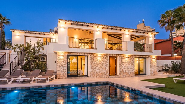 Une maison à deux étages avec une piscine, une façade en pierre et un espace salon extérieur.
