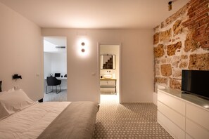 Une chambre d’hôtel moderne, équipée d’un lit, d’une télévision, d’un mur décoratif en briques et d’une salle de bain visible à travers une porte ouverte.