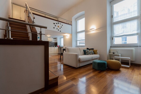 A modern living room with a wooden staircase, a white sofa, and a large window.
