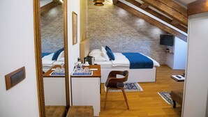 A bedroom with a loft bed, wooden beams, a brick wall, a small desk with a mirror, and a TV mounted on the wall. - Oblivion rooms (Split)