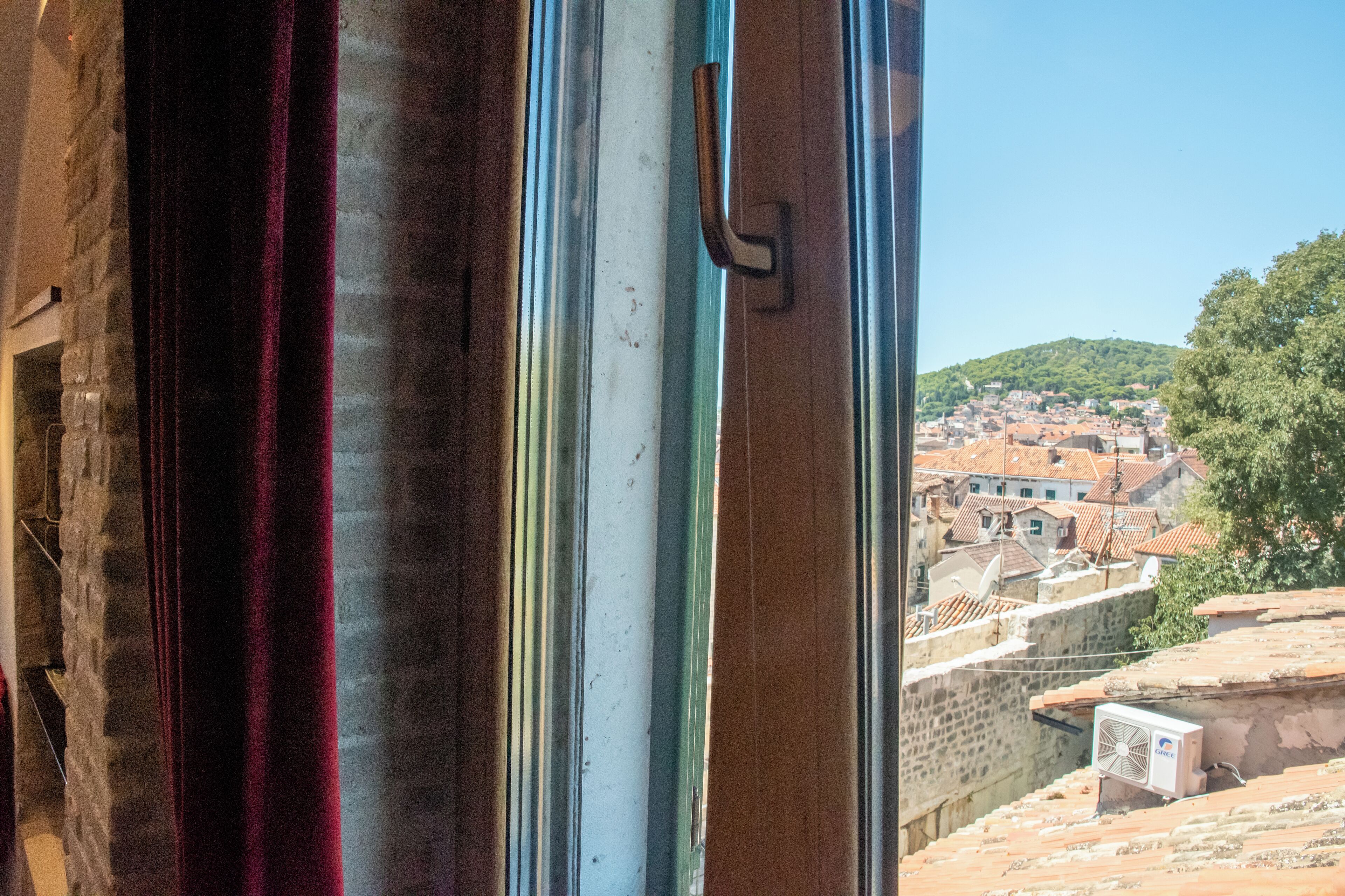 A window with a view of a town with buildings and a hill in the background.