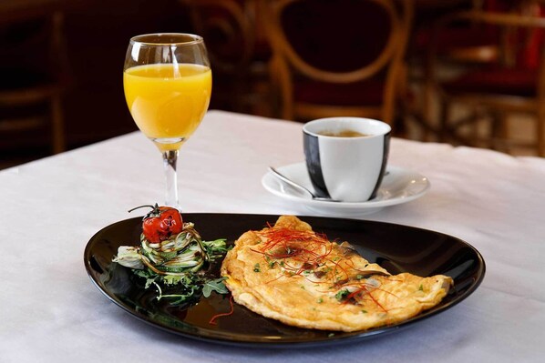 A dining table with a plate of food, a glass of orange juice, and a cup of coffee.