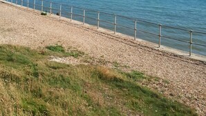 Une promenade en bord de mer avec une rambarde en métal, des galets et de l’herbe.