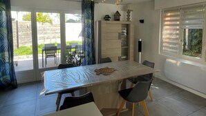 A dining area with a table, chairs, a ceiling light fixture, and a view of the outdoors through large windows. - Maison Familiale Avec Jardin (Avelin)