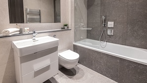 Et moderne badeværelse med et glasafskærmet brusebad, en hvid vask og et toilet.