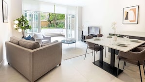En moderne stue med sofa, spisebord og stole. Der er et stort vindue med udsigt over det fri.