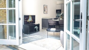 En moderne stue med et fladskærms-tv, grå sofaer, et spiseområde med bord og stole, og et køkken i baggrunden.