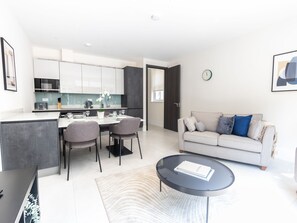 A modern living room with a sofa, coffee table, and dining area with chairs and a table. - Little Venice Charm Cozy One-bedroom by Sojo Stay (London)