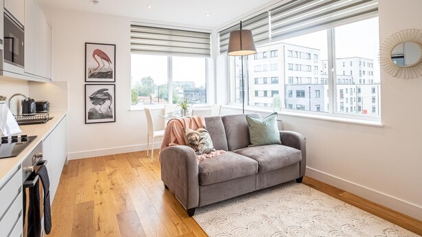 A modern apartment with a kitchen, grey sofa, and large windows offering city views. - Two-bedroom Near Cliveden House by Belvilla (Slough)