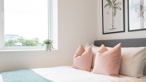 A neatly made bed with a teal throw blanket and pink pillows, a window with a view of buildings, and two framed botanical prints on the wall. - Two-bedroom Near Cliveden House by Belvilla (Slough)