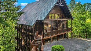 A log cabin with a metal roof, wooden deck, and a staircase leading to the entrance.