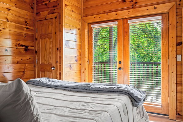 A wooden cabin room with a bed, a door, and a window with blinds.