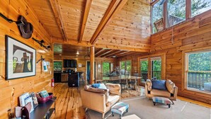 A spacious wooden cabin with a dining area, a kitchen, and a cozy seating area with a fireplace.