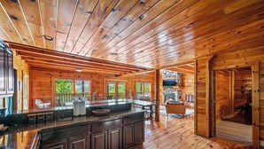 A spacious wooden cabin with a large kitchen area, a dining table, and a fireplace.