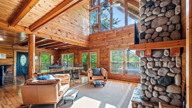 A spacious wooden cabin with a stone fireplace, large windows, and a dining area.
