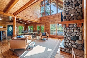 A spacious wooden cabin with a stone fireplace, large windows, and a dining area.