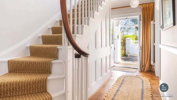 Un escalier recouvert d’une moquette à motifs, avec des rampes blanches et une main courante en bois.