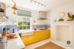 A modern kitchen with yellow cabinets, a white countertop, a window with blue patterned curtains, a sink, and a stove. - Nothe House - Exclusive home, Weymouth Harbour (Weymouth)