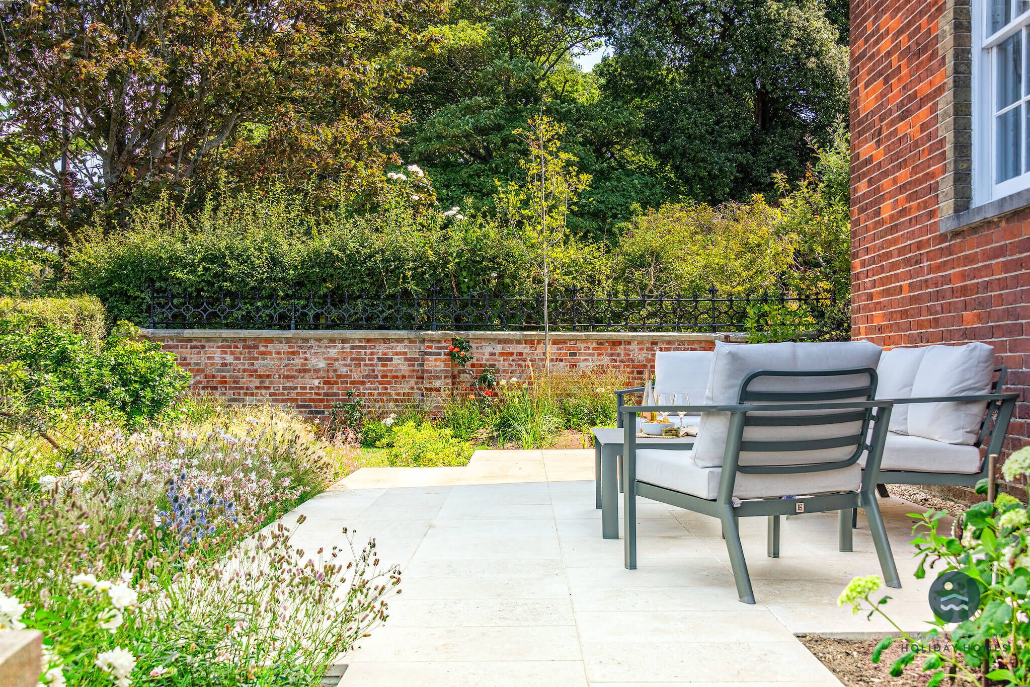 A patio with a table and chairs, surrounded by a brick wall and lush greenery.
