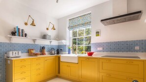 Une cuisine avec des meubles de couleur jaune, un plan de travail blanc et une fenêtre agrémentée de rideaux à motifs.