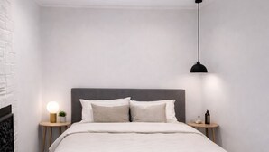 Une chambre moderne avec un lit, des tables de chevet, une lampe fixée au mur et un luminaire au plafond.