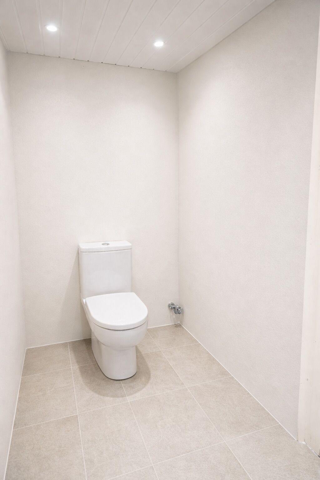A small, white bathroom with a toilet, tiled floor, and white walls.