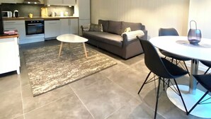 Un salon moderne comprenant un canapé, une table à manger avec des chaises, un coin cuisine équipé d’appareils électroménagers et un tapis sur le sol.