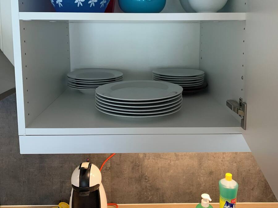 Armário de cozinha com prateleiras contendo pratos, tigelas e uma cafeteira.