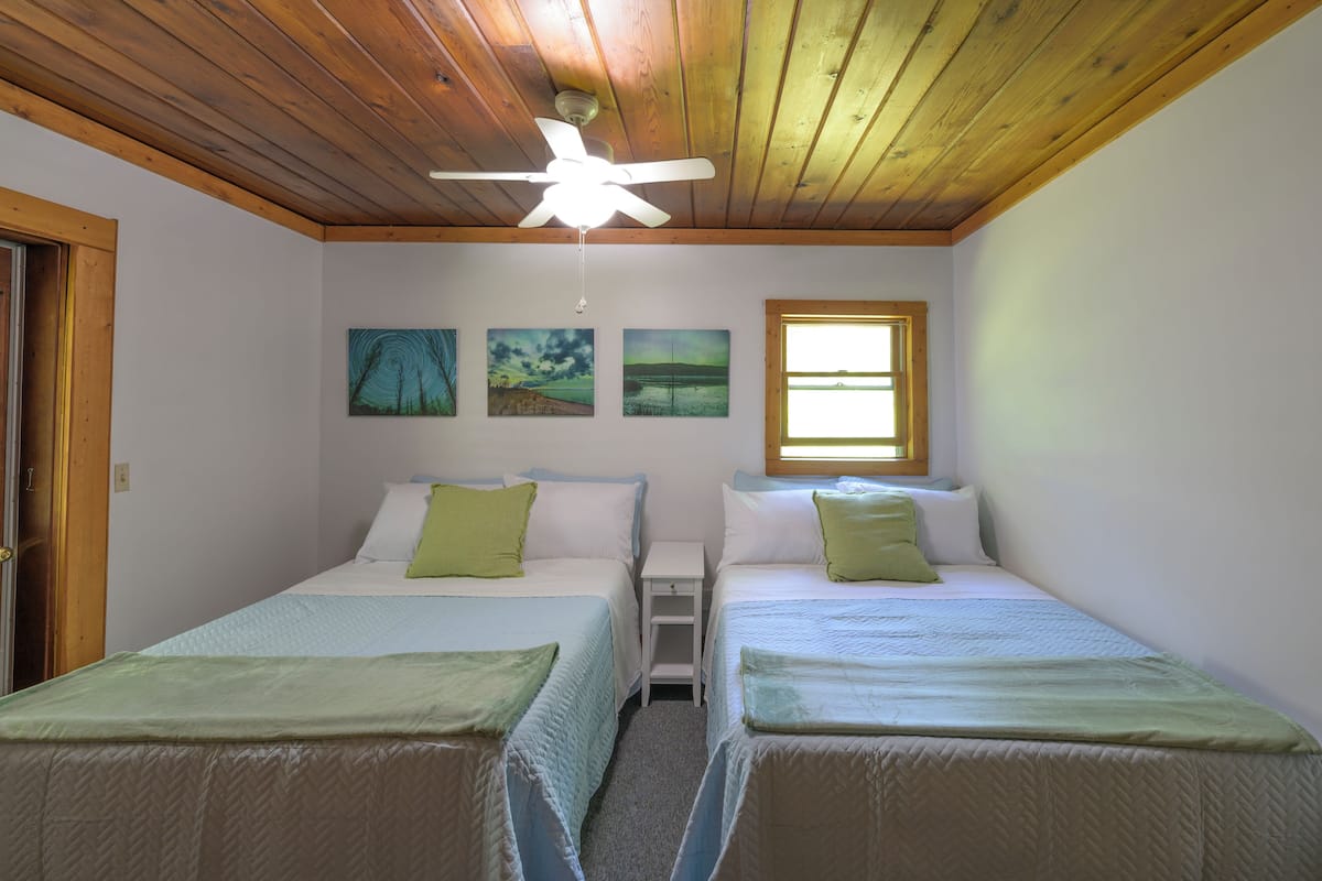 A bedroom with two beds, a ceiling fan, and three paintings on the wall.