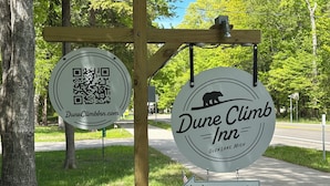 A wooden signpost with two circular signs for Dune Climb Inn, a QR code, and a vacancy arrow.