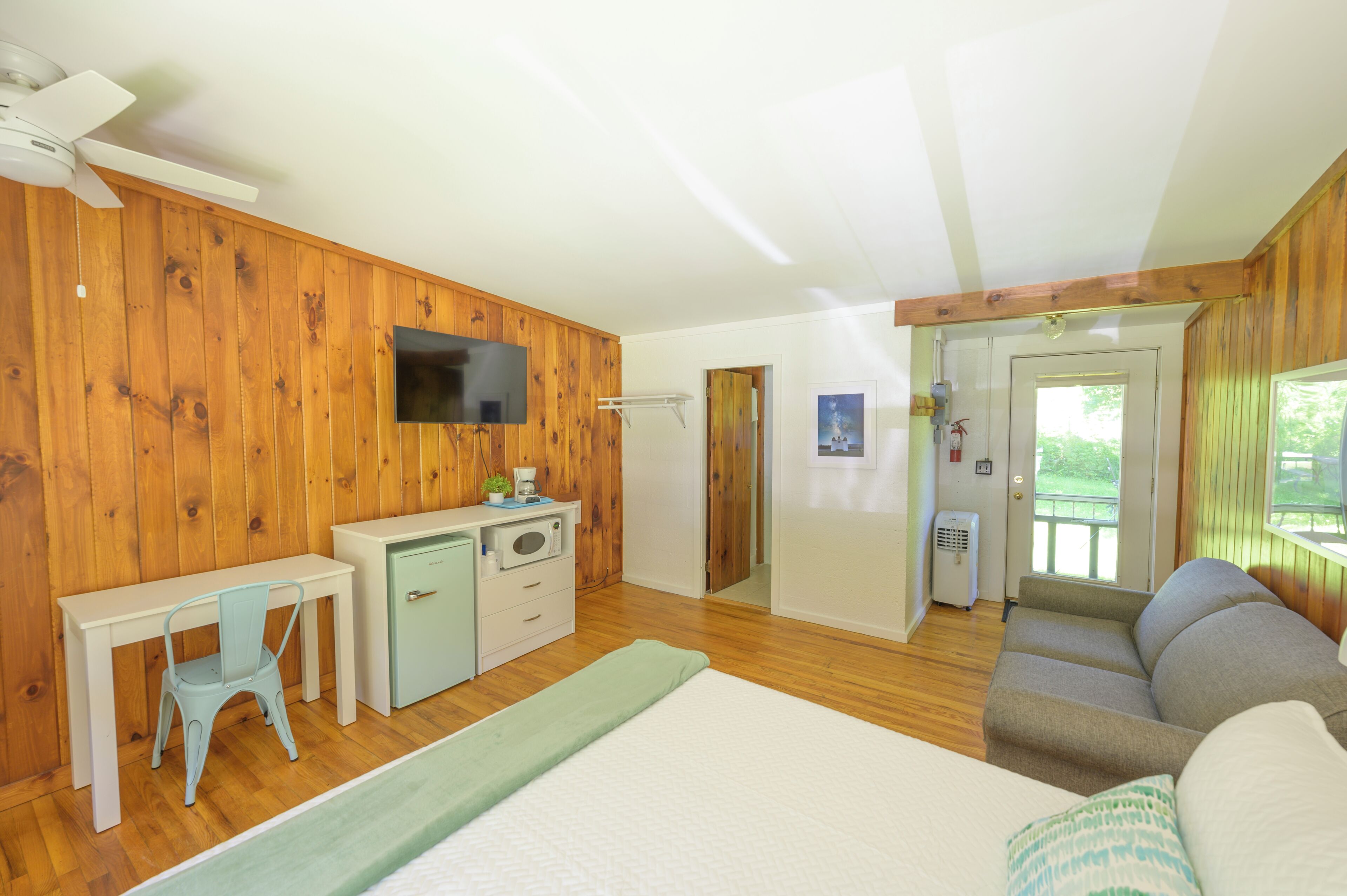 Una habitación con cama, escritorio, sillón, sofá y televisor.