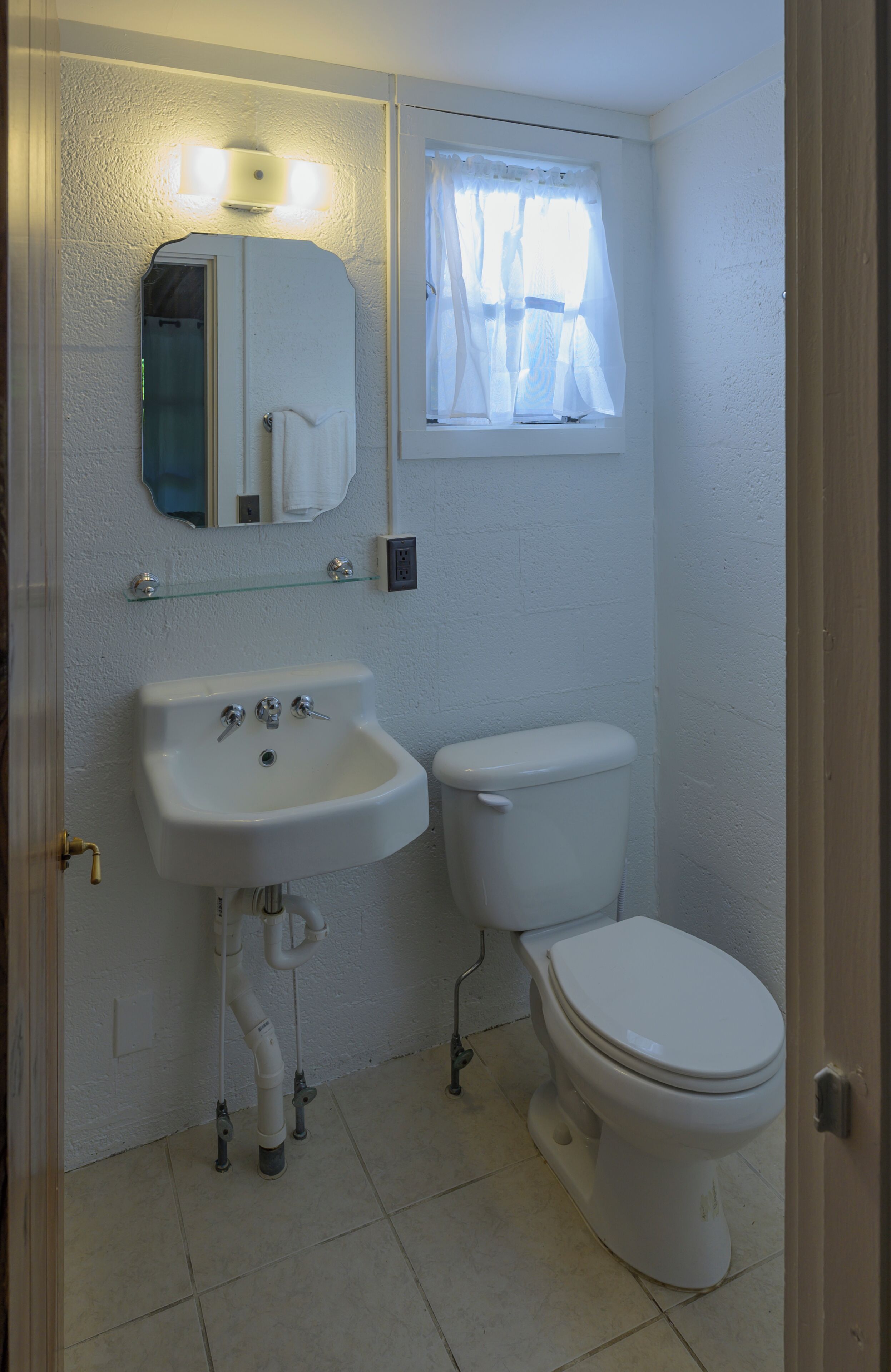 A small bathroom with a white sink, a toilet, and a window with sheer curtains.
